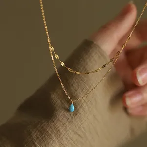 Detailed macro view of a golden double-layered necklace with a blue teardrop resin pendant.