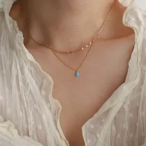Detail view of double-layered gold necklace with blue teardrop opal pendant on model neck