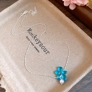Vue détaillée d'un pendentif fleur bleue avec perle blanche sur un collier en argent fin
