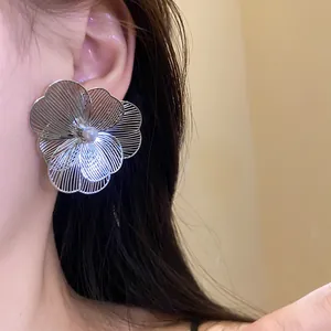Close-up detail of a large silver hollow flower earring with pearl center worn on ear