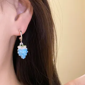 Detail view showing a charming blue enamel strawberry drop earring worn on model's ear