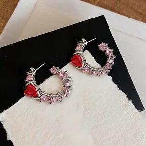 Detailed macro view of pink zircon C-shaped hoop earrings with a red heart-shaped gemstone