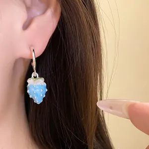 Detailed view of a light blue enamel strawberry pendant hoop earring worn on an ear