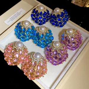 Primer plano de pendientes vintage con piedras de colores y perlas en estuche de lujo.