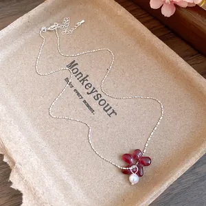 Gros plan d'un collier en chaîne argentée avec fleur en résine rouge et perle