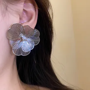 Macro view of large silver metal flower earring with a white pearl center on ear