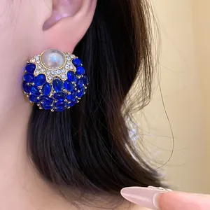 Vista detallada de pendientes de botón vintage con piedras azules y perla central