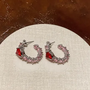 Detailed macro view of elegant silver C-shaped hoop earrings with red heart zircons