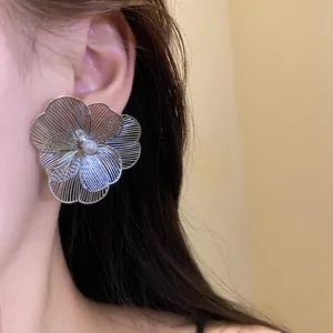Detail view of a large metal flower earring with a central pearl on a model's ear