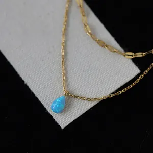 Close-up of a double-layered gold necklace with a vibrant blue teardrop pendant