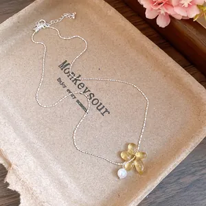 Gros plan détaillé du pendentif fleur jaune translucide et perle sur une chaîne argentée fine