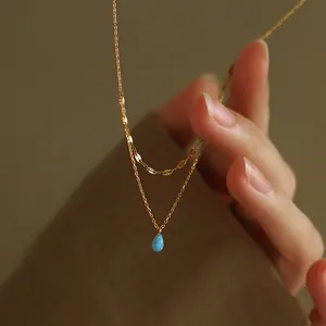 Close-up of elegant double-layered gold stainless steel necklace with a blue teardrop pendant
