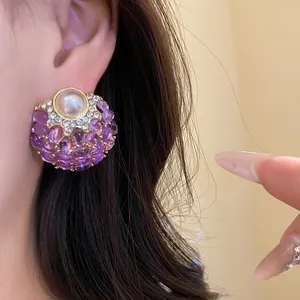 Detalle de un pendiente vintage con gemas moradas y una perla central en la oreja.
