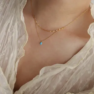 Close-up of double-layered gold necklace with blue teardrop pendant on lace blouse.