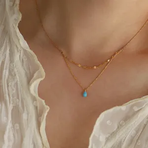 Close-up detail of a double-layered gold necklace with a vibrant blue teardrop pendant