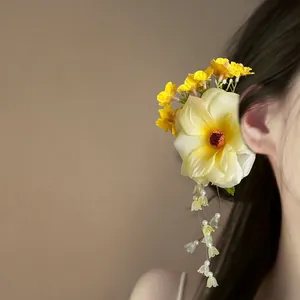 Detailed view of yellow fabric flower hair clip with elegant hanging bead tassels.