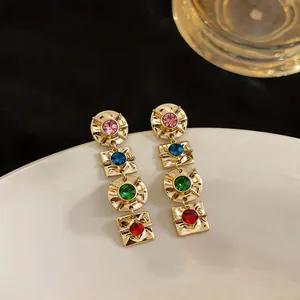 Macro detail of vintage-style geometric gold-tone earrings with multi-colored gemstones