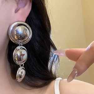 Detailed view of three-tier metallic mirror-finish round drop earrings worn by model