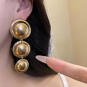 Detail showing macro view of tiered gold-tone glossy metal round drop earrings worn on ear