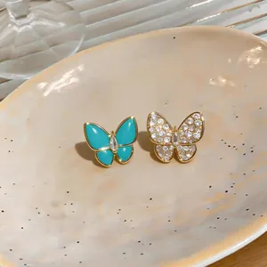 Close-up detail of asymmetric butterfly stud earrings with pavé zircon and turquoise resin
