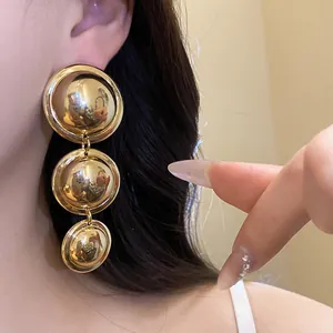 Close-up of vintage minimalist three-tiered gold metallic drop earrings worn by a model