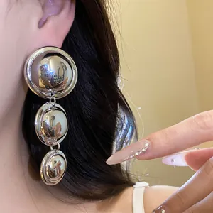 Detailed close-up showing a metallic round tiered dangle earring being worn on an ear