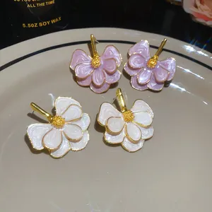 Detailed view of pink and white enamel flower stud earrings on a ceramic plate