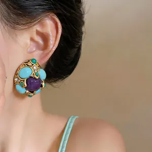 Primo piano di orecchini vintage geometrici con pietre turchesi e viola su modella