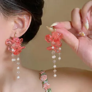 Detail shot of elegant coral flower earrings with pearl tassels worn on a model.