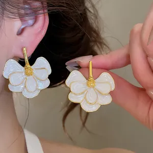 Close-up view of elegant white enamel flower earrings featuring intricate gold accents