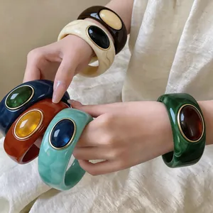 Detailed view of chunky marbled acrylic bangles with elegant oval gemstone inlays.