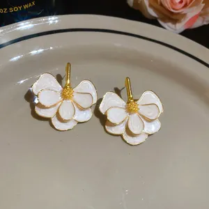 Close-up view of elegant white enamel flower stud earrings with gold-tone petal centers.