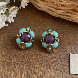 Primo piano di orecchini vintage a fiori con pietre turchesi e viola su superficie legno