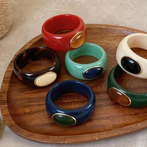 Group of colorful chunky acrylic bangles with oval resin insets on a wooden tray