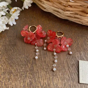 Detail view of red floral tassel earrings with faux pearls on wooden surface.