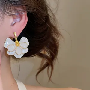 Macro close-up of an elegant white enamel flower stud earring with gold-toned details