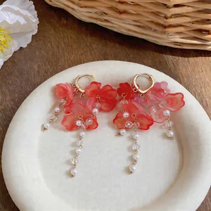 Detailed view of red floral tassel earrings with faux pearls and gold hoops on a tray