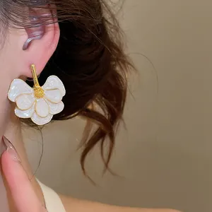 Detail shot of elegant white enamel flower earrings with gold trim on a model's ear