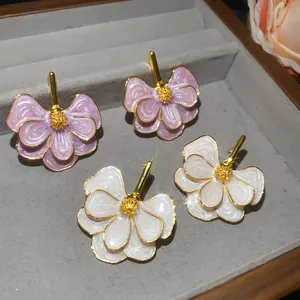 Close-up of elegant enamel flower stud earrings in lavender and white colors.