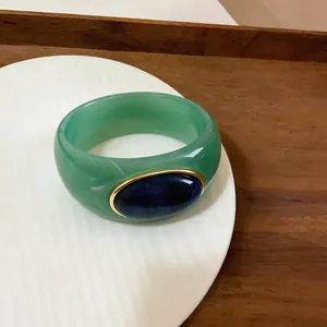 Macro view of a green acrylic marbled bangle with a navy blue oval inset.