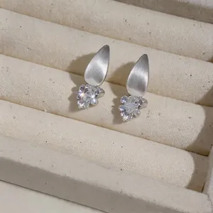 Close-up detail of French minimalist teardrop zircon stud earrings in a beige jewelry box