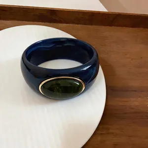 Detail of a chunky navy marbled acrylic bangle with green stone and gold frame
