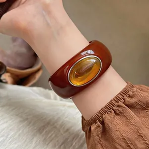 Close-up of a stylish reddish-brown acrylic bangle with amber stone detail on a wrist