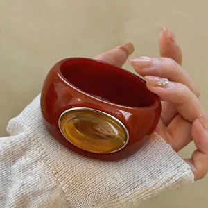 Close-up of a chunky red acrylic bangle featuring a large oval amber stone detail.