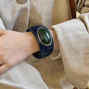 Detailed view of an oversized navy blue acrylic bangle with a green resin centerpiece