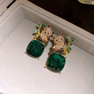 Detail shot of diamond-encrusted panda earrings with green square gemstone pendants