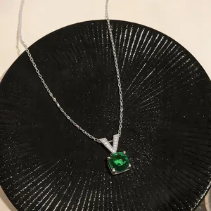 Dettaglio macro di una collana in argento con gemma verde rotonda e chiusura a V.