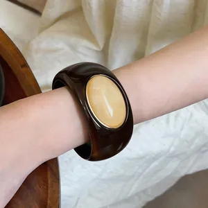 Close-up of a chunky brown acrylic bangle with a cream marbled oval inlay on wrist.