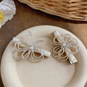 Primo piano di eleganti fermagli per capelli a fiore cavo con perle su un piatto di ceramica