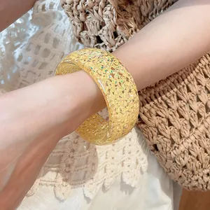 Close-up of yellow resin bangle with glitter inclusions worn on wrist with straw bag